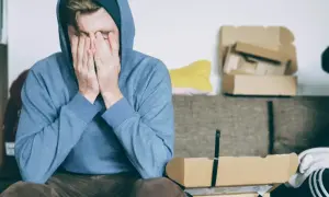 Mężczyzna w bluzie z kapturem, z rękami na twarzy, symbolizuje wyuczoną bezradność.