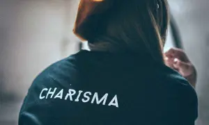 Osoba w bluzie z napisem "CHARISMA" na plecach, z włosami opadającymi na ramiona i dłonią przy uchu.