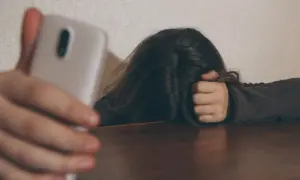 Osoba z telefonem w dłoni, ukrywająca twarz we włosach. Czy to próba ukrycia smutku, czy tylko pozowanie? Człowiek dwulicowy.