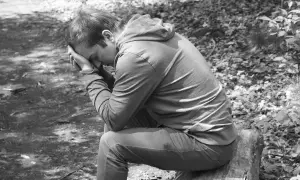 Chłopak siedzi na pniu, pogrążony w myślach. Jego twarz ukryta w dłoniach, symbolizuje głęboką żałobę po mamie.