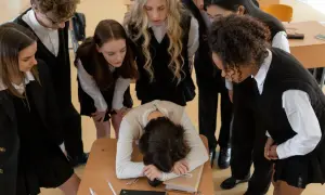 Uczniowie patrzą na skuloną koleżankę przy ławce. Scena pokazuje, czym jest bullying.