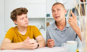 Ojciec tłumaczy synowi, jak rozmawiać z nastolatkiem, używając gestów. Chłopiec słucha uważnie.