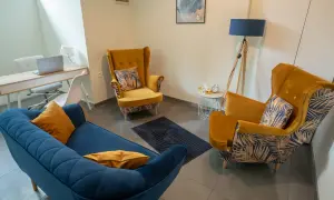 Gabinet psychologa: niebieska kanapa, dwa żółte fotele, biurko z laptopem, lampa.