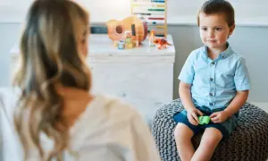 Chłopiec w niebieskiej koszuli siedzi na pufie, rozmawiając z psychoterapeutką.