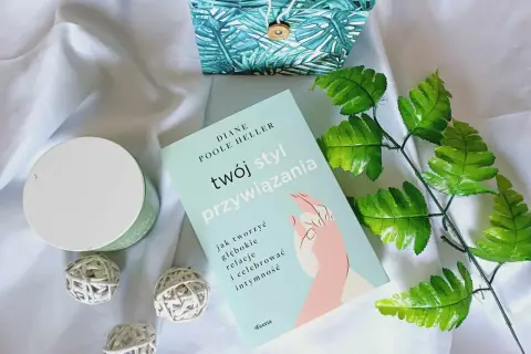 Książka "Twój styl przywiązania" Diane Poole Heller na tle białego materiału, obok ozdobnego pudełka i zielonych liści.
