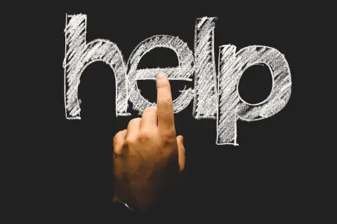 Palec wskazuje literę "e" w napisie "help" na tablicy. To symboliczne wezwanie o pomoc, często pojawiające się w kontekście psychologii rozwojowej.