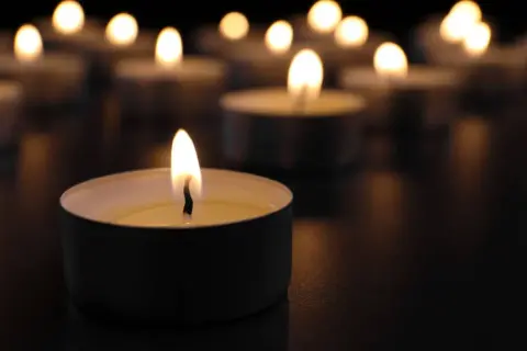 Płonące świece w ciemności, symbolizujące żałobę i pamięć.