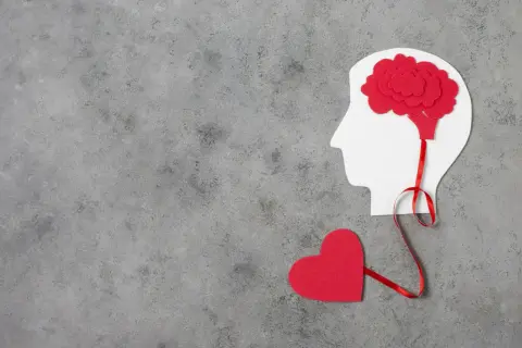 Czerwone serce połączone wstążką z mózgiem w profilu głowy. Symbolizuje to emocjonalne reakcje neurotyka.