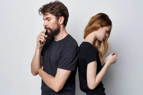Para stojąca plecami do siebie, oboje patrzą w telefony. On zamyślony, ona zrezygnowana. Cisza między nimi to wyraźny **silent treatment**.