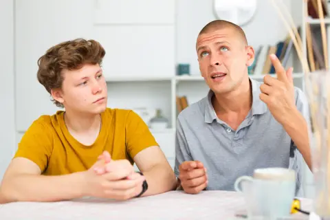 Ojciec tłumaczy synowi, jak rozmawiać z nastolatkiem, używając gestów. Chłopiec słucha uważnie.