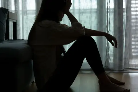 Sylwetka kobiety siedzącej na podłodze, z ręką na czole, odzwierciedla **epizod depresyjny** i walkę z **depresją**.