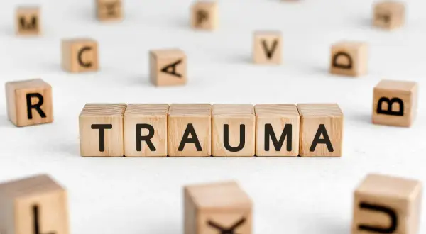Drewniane klocki układają się w słowo TRAUMA, otoczone innymi literami. To obraz symbolizujący trudne doświadczenia.