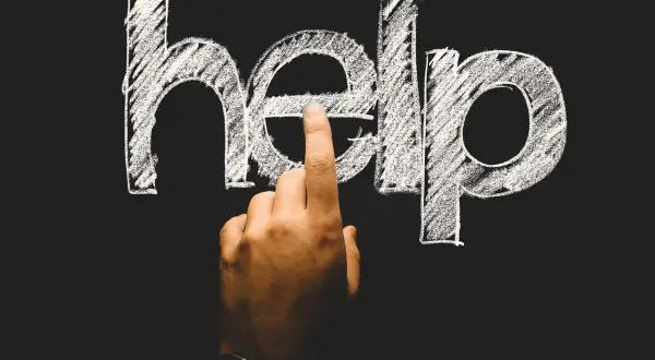 Palec wskazuje literę "e" w napisie "help" na tablicy. To symboliczne wezwanie o pomoc, często pojawiające się w kontekście psychologii rozwojowej.