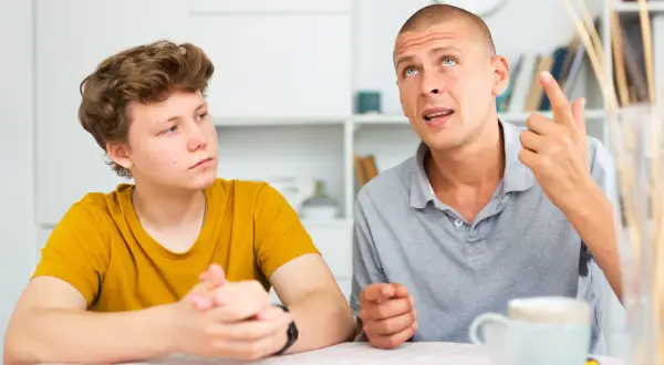 Ojciec tłumaczy synowi, jak rozmawiać z nastolatkiem, używając gestów. Chłopiec słucha uważnie.