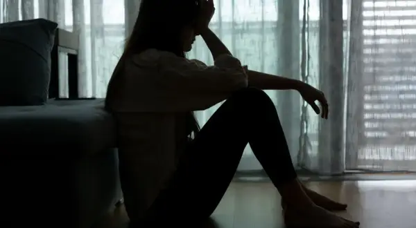 Sylwetka kobiety siedzącej na podłodze, z ręką na czole, odzwierciedla **epizod depresyjny** i walkę z **depresją**.