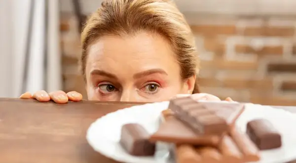 Kobieta z uwagą spogląda na talerz z czekoladą, co może symbolizować jedzenie emocjonalne.
