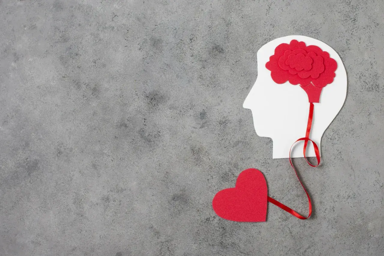 Czerwone serce połączone wstążką z mózgiem w profilu głowy. Symbolizuje to emocjonalne reakcje neurotyka.