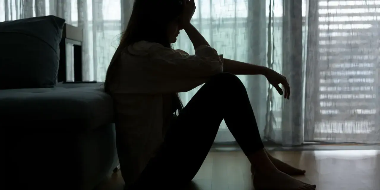 Sylwetka kobiety siedzącej na podłodze, z ręką na czole, odzwierciedla **epizod depresyjny** i walkę z **depresją**.
