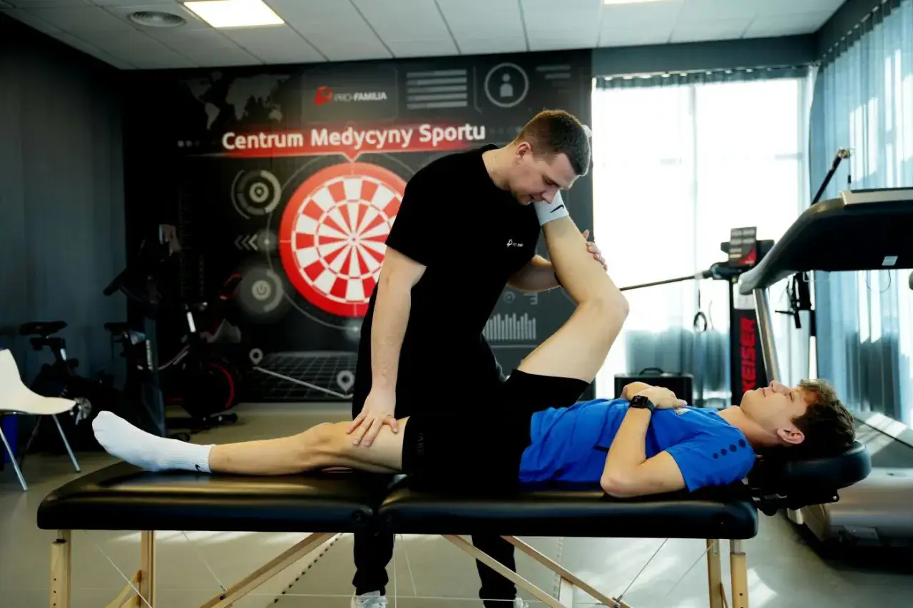 Fizjoterapeuta wykonuje ćwiczenia z młodym sportowcem na kozetce w centrum medycyny sportowej.