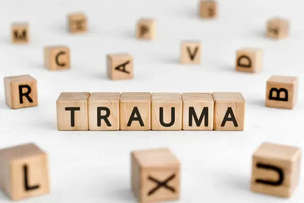 Drewniane klocki układają się w słowo TRAUMA, otoczone innymi literami. To obraz symbolizujący trudne doświadczenia.