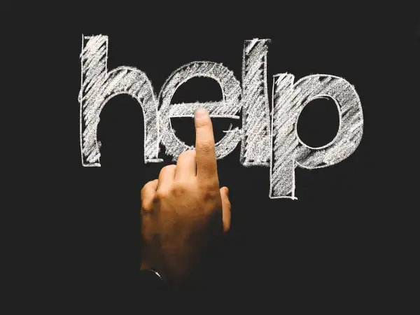 Palec wskazuje literę "e" w napisie "help" na tablicy. To symboliczne wezwanie o pomoc, często pojawiające się w kontekście psychologii rozwojowej.
