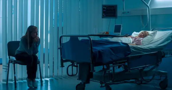 Zmartwiona matka siedzi obok śpiącego dziecka w szpitalnym łóżku, co może sugerować zespół Münchhausena u matek.