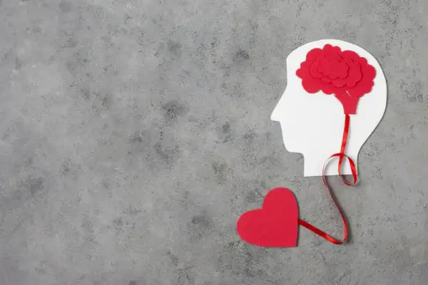 Czerwone serce połączone wstążką z mózgiem w profilu głowy. Symbolizuje to emocjonalne reakcje neurotyka.