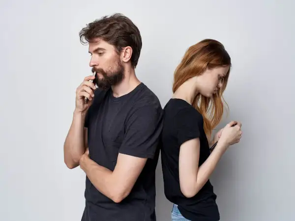 Para stojąca plecami do siebie, oboje patrzą w telefony. On zamyślony, ona zrezygnowana. Cisza między nimi to wyraźny **silent treatment**.
