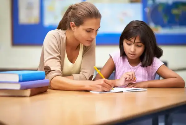 Nauczycielka pomaga uczennicy w pisaniu, wspierając ją w procesie edukacyjnym, który może być częścią orzeczenia z poradni psychologiczno-pedagogicznej.