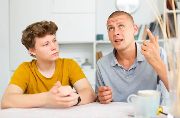 Ojciec tłumaczy synowi, jak rozmawiać z nastolatkiem, używając gestów. Chłopiec słucha uważnie.