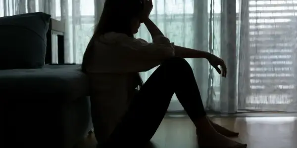 Sylwetka kobiety siedzącej na podłodze, z ręką na czole, odzwierciedla **epizod depresyjny** i walkę z **depresją**.